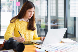 Frau sitzt vor einem Laptop mit einem Stift in der Hand